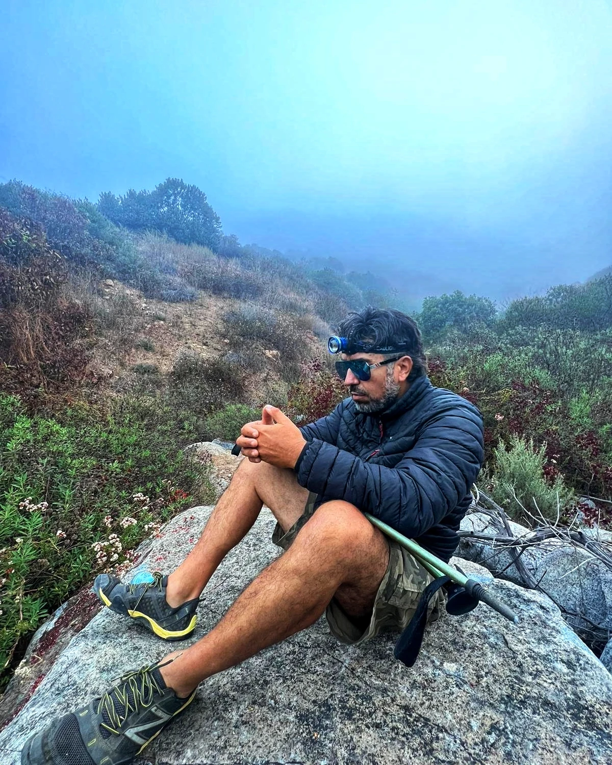 A hiker seated quietly on a rock in misty mountain terrain